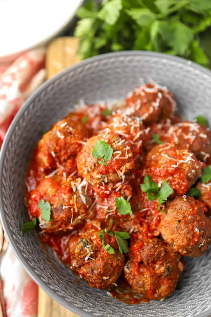 baked meatballs in a grey bowl topped with Parmesan and parsley.