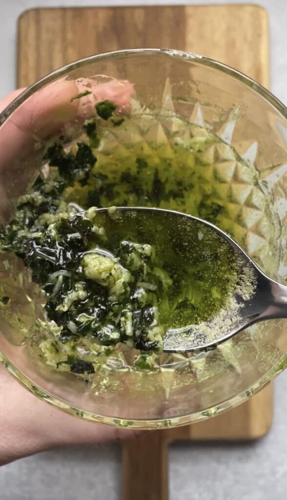 a spoon showing the basil garlic butter with a glass bowl.