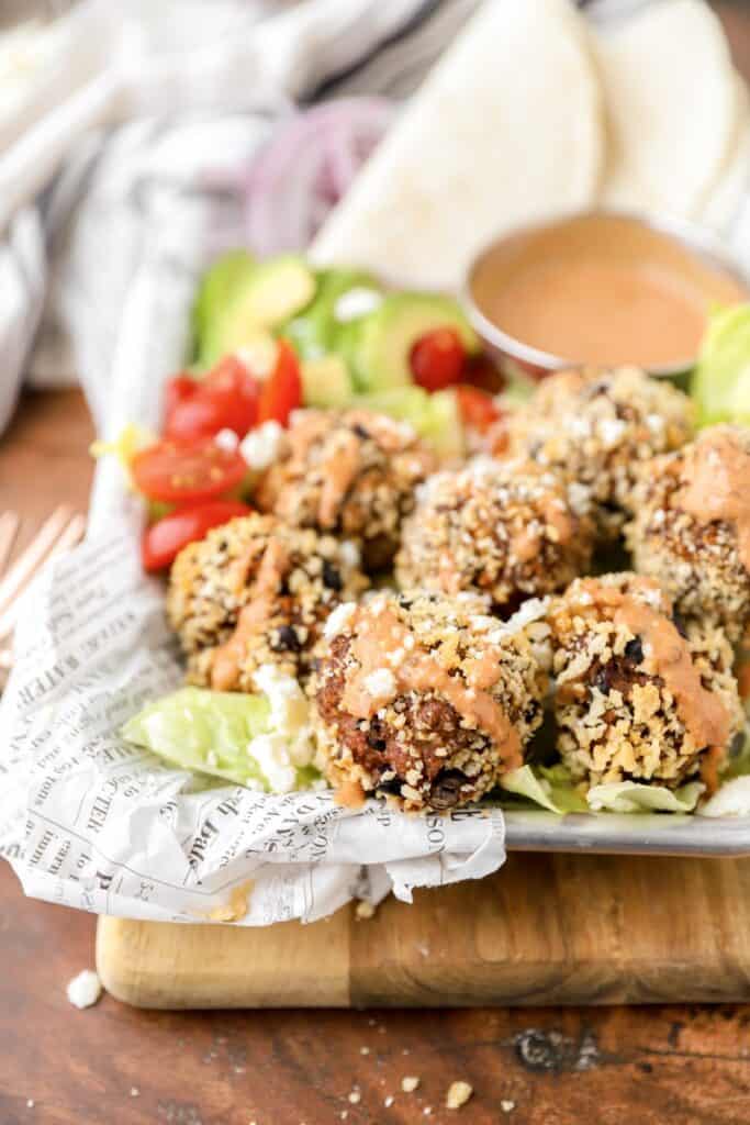 taco meatballs on a metal tray with avocado, tomatoes, and a chipotle sauce.