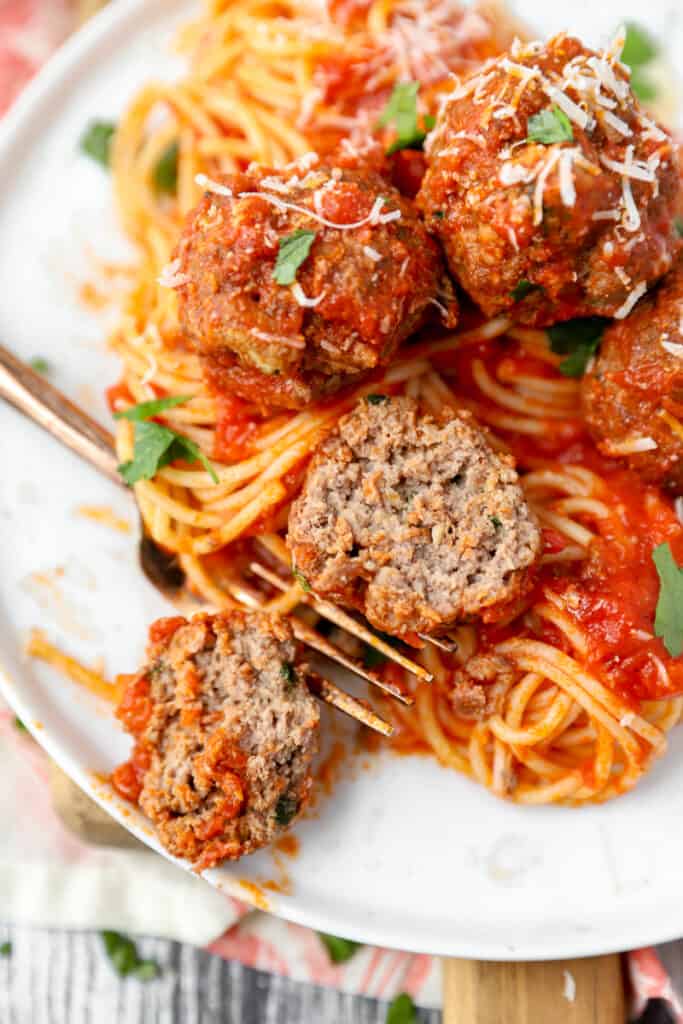 close shot of one of the meatballs cut open to show the texture of the interior, on a white plate with a bronze fork.