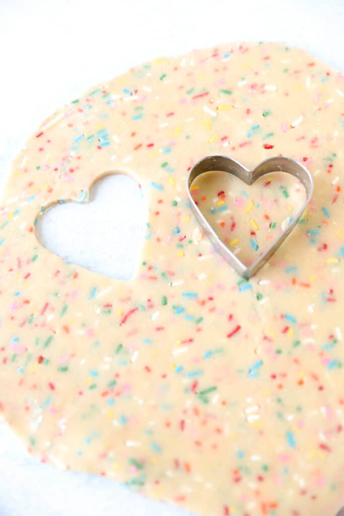 rolled out raw cookies dough with a heart shaped cut out, heart shaped cutter to the side.