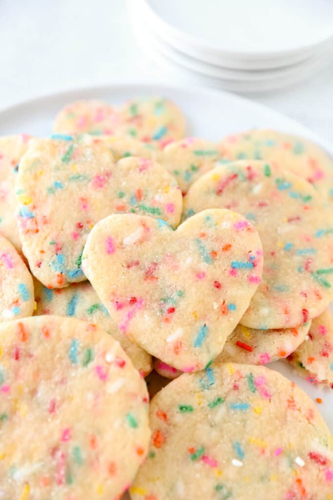 pile of the chewy sprinkle cookies with a heart shaped one on top.