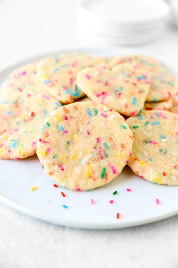 a pile of sprinkle cookies on a white round plate