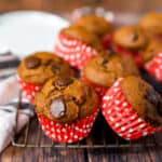 pumpkin chocolate chip muffins in polka dot wrappers on a baking rack on a wood surface.