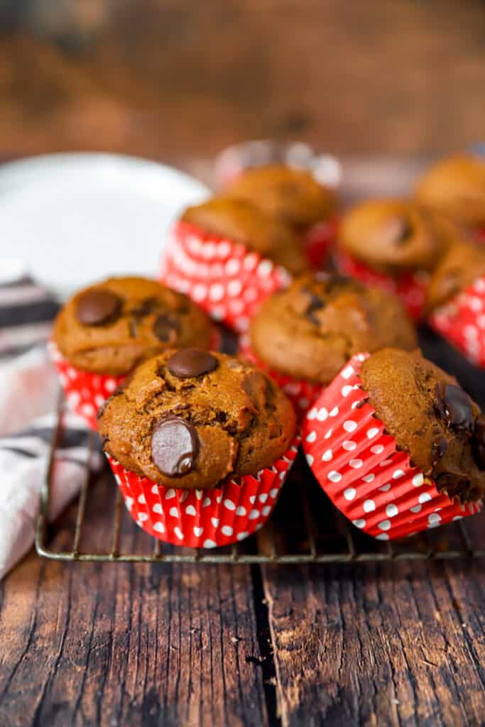 pumpkin chocolate chip muffins in polka dot wrappers on a baking rack on a wood surface.