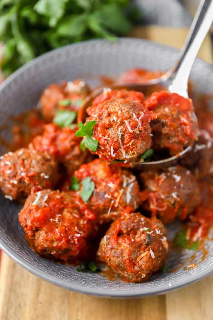 a stainless steel ladle scooping the meatballs from the grey bowl.