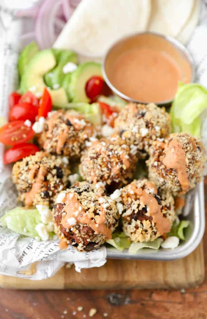 overhead shot of the taco meatballs on a tray with diced tomatoes, lettuce, avocado and a drizzled chipotle crema.