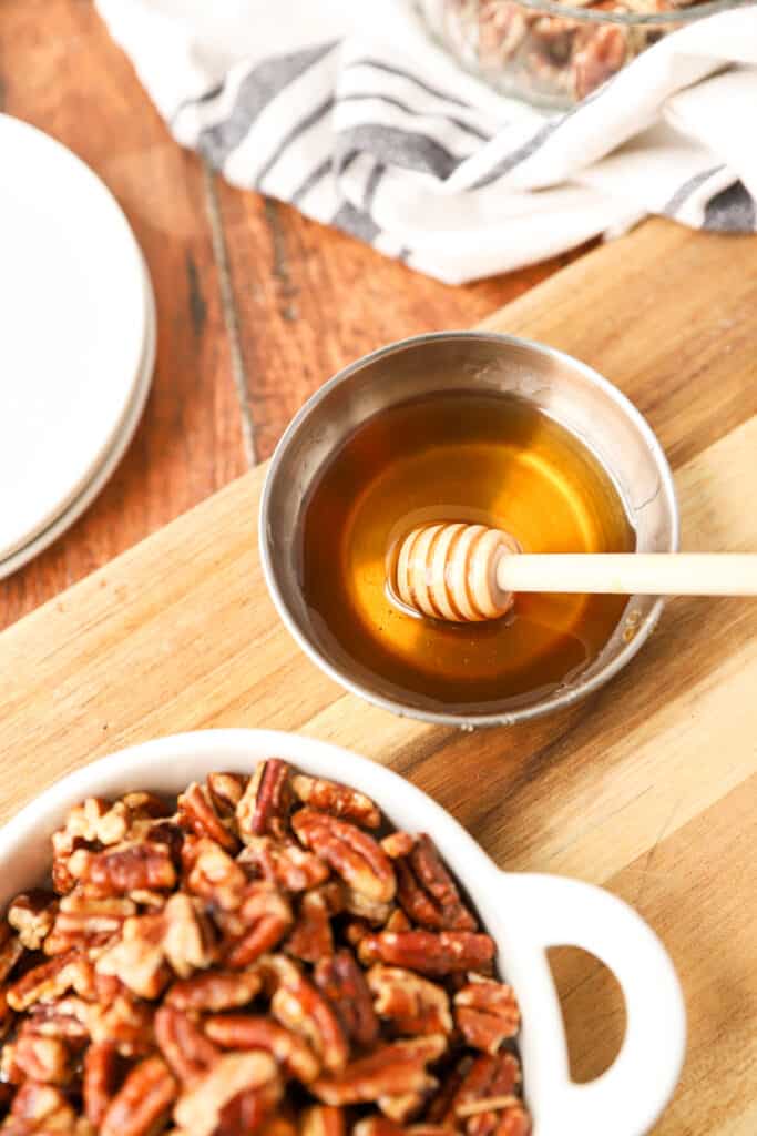 a small silver dish with honey and a small wooden honey dipper on a wood cutting board.