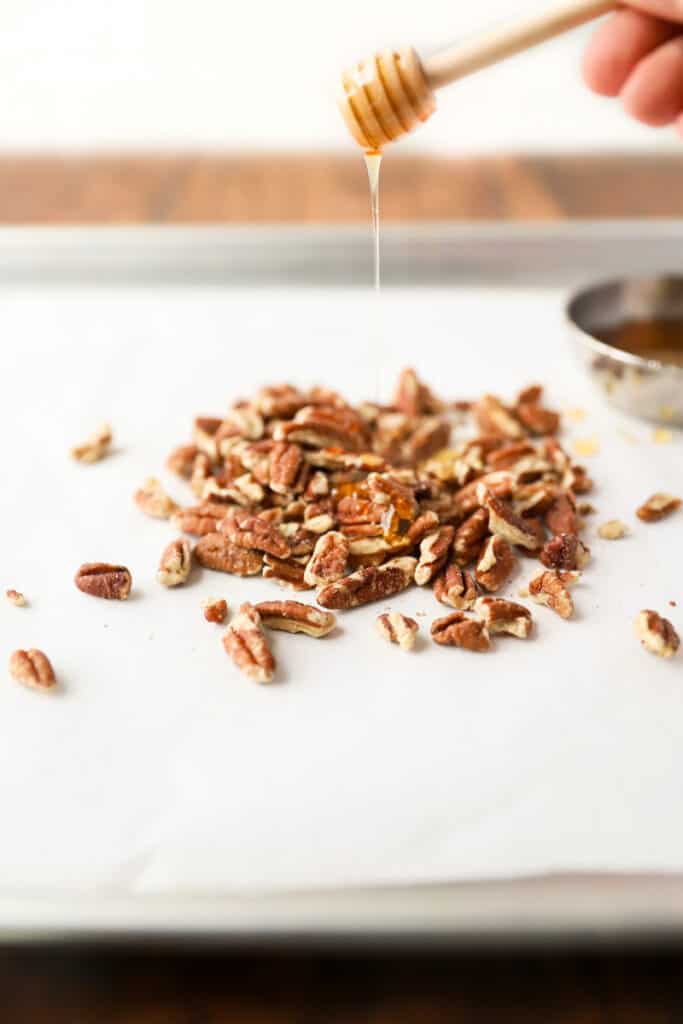 the chopped pecans on parchment paper with honey being drizzled on them.