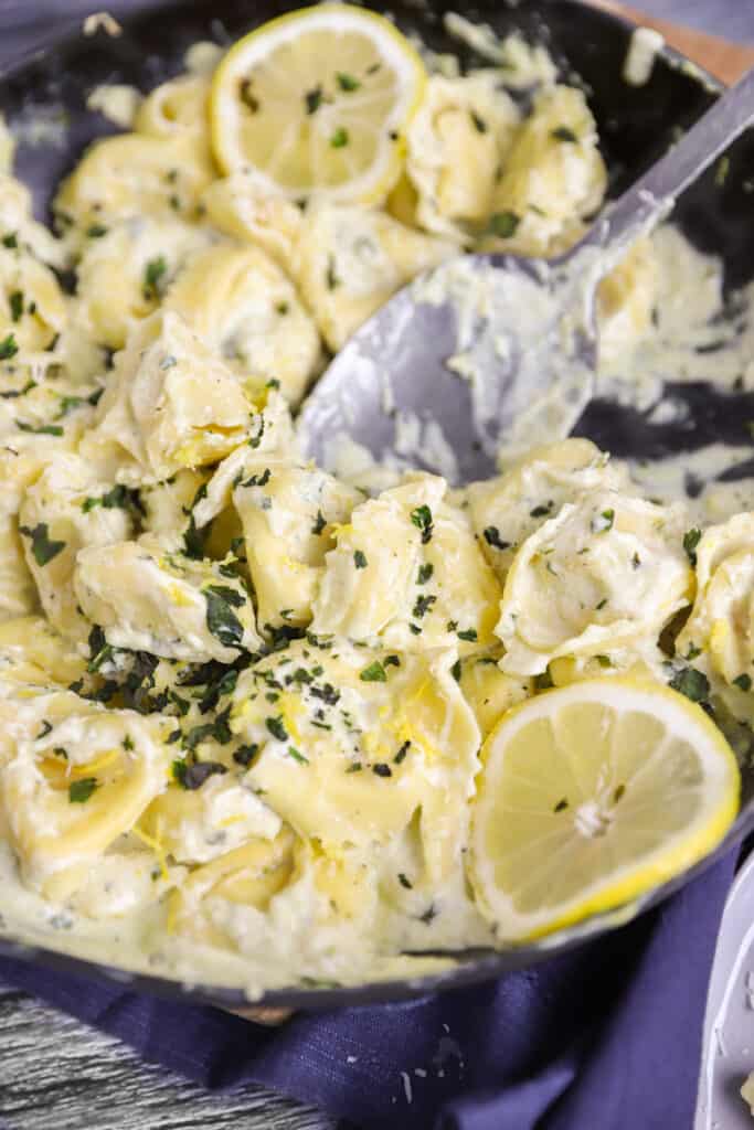 pan of lemon basil tortellini with lemons slices and a silver spoon.