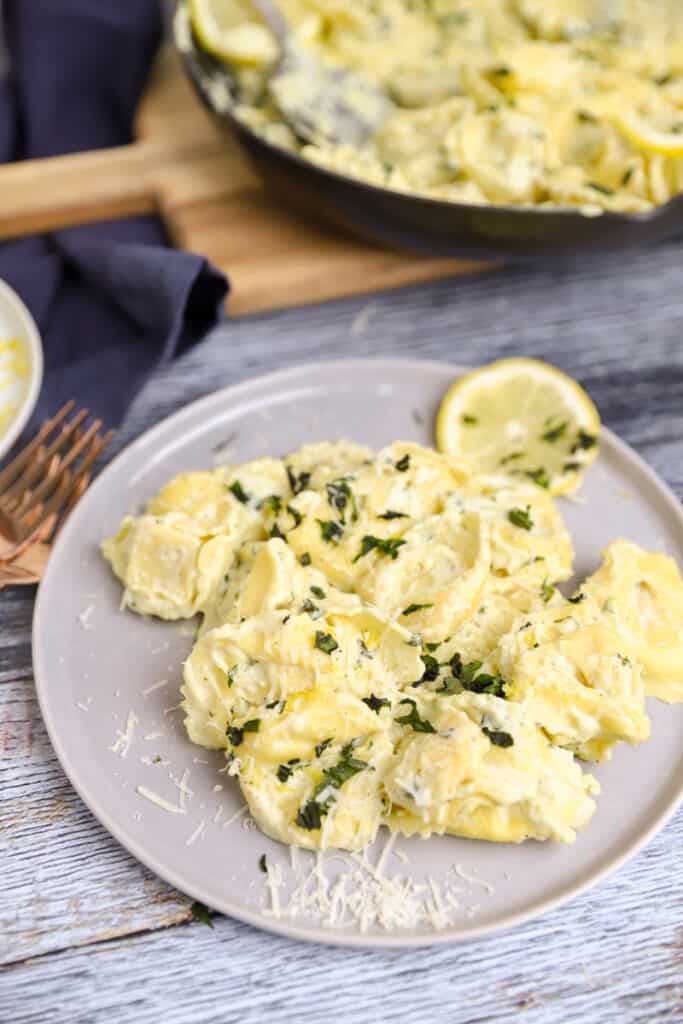 a plate of the lemon basil tortellini on a grey round plate with forks and a blue napkin.