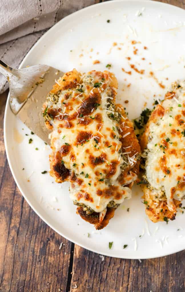 a silver spatula placing one of the finished chicken parms on a large white round plate.