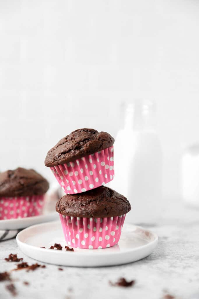 two muffins in pink polka dot wrappers stacked on top of each other on a small round white plate.