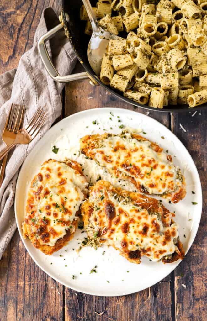 a large round white plate with three pesto chicken parms on a wood surface,