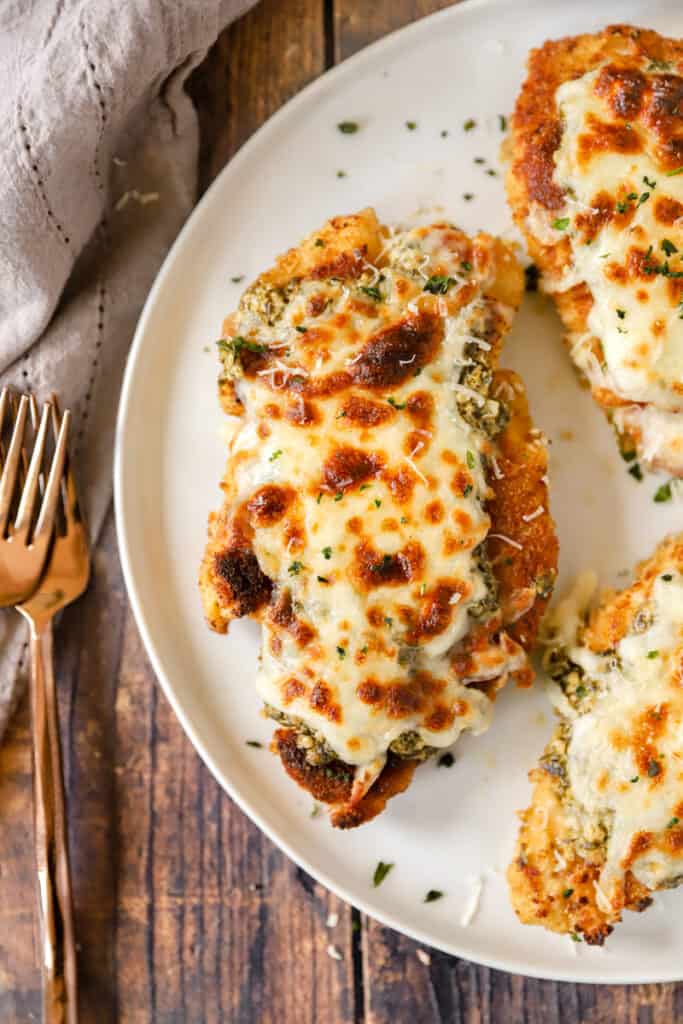 overhead shot of the pesto chicken parm on a white plate with two forks.