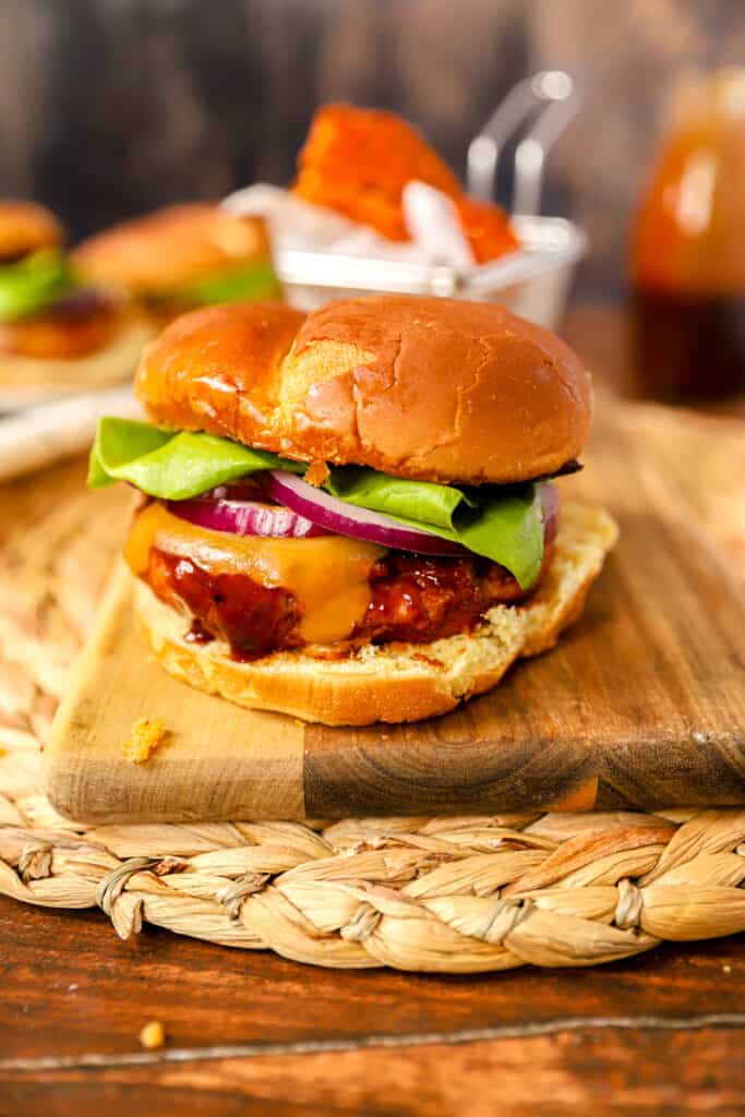 bbq chicken burger on a wood cutting board on a wood surface. Sweet potato fries in the backhground.