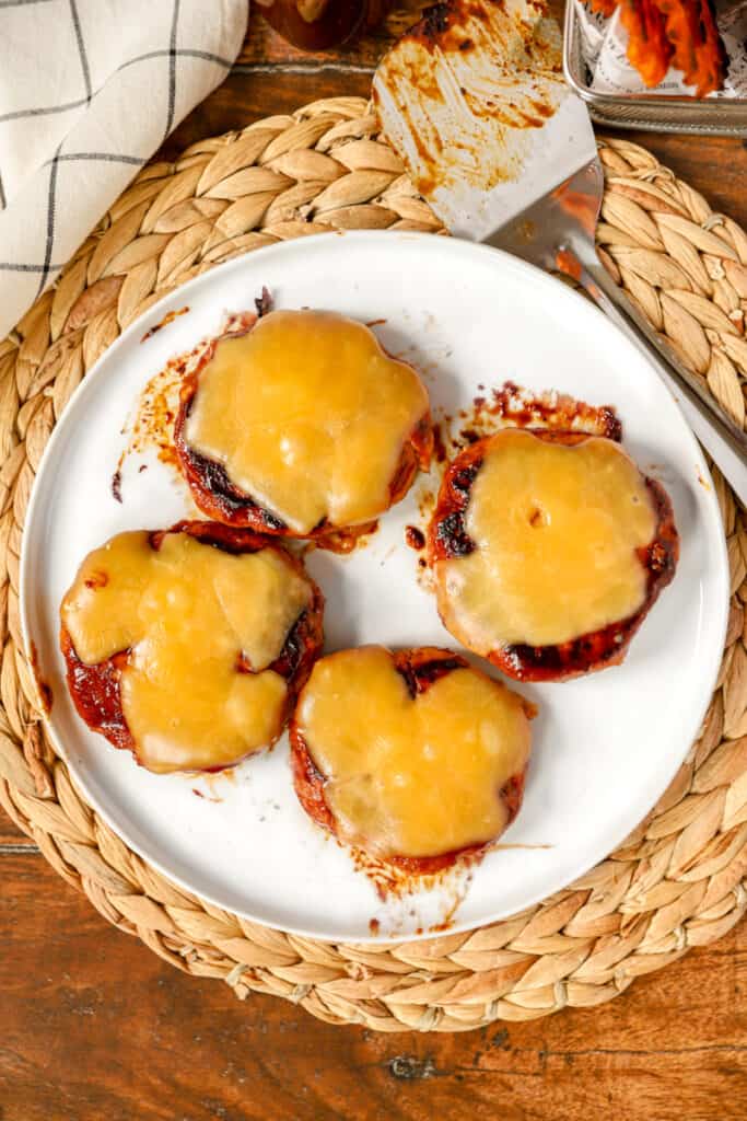 overhead shot of 4 BBQ chicken burgers on a round white plate on a rattan placemat.