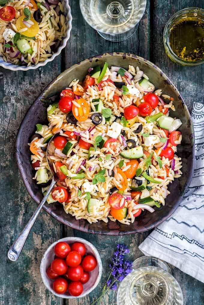 overhead shot of the Greek orzo pasta salad on a blueish wood surface with a large silver spoon.