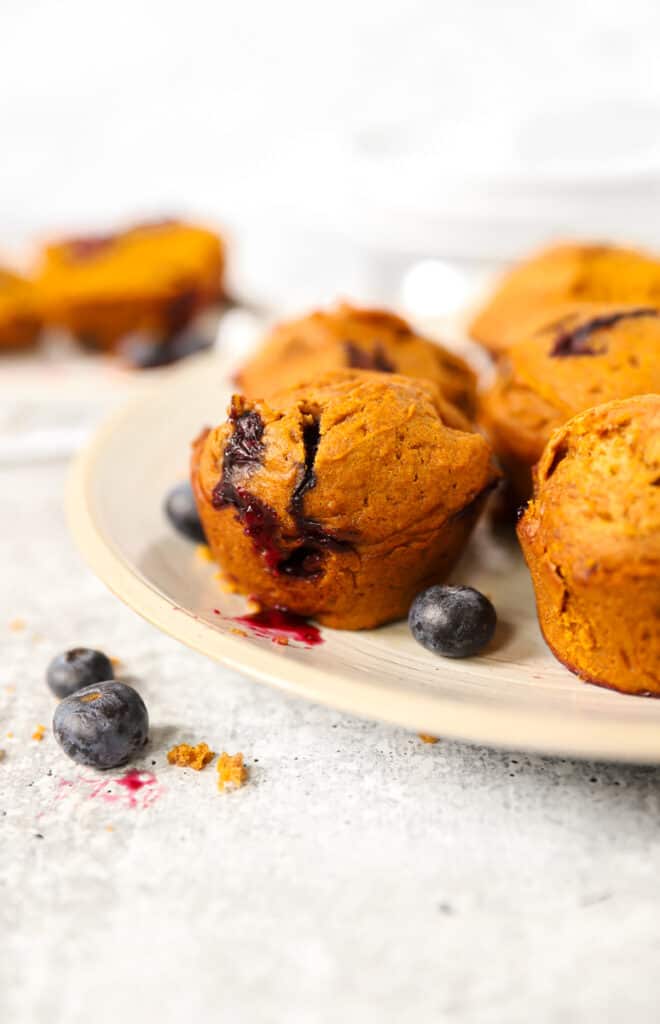 pumpkin blueberry muffins on a white plate with scattered blueberries