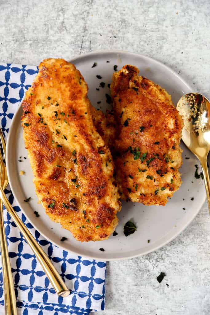 overhead shot of the cooked dredged and breaded chicken on a grey plate with gold utensils.