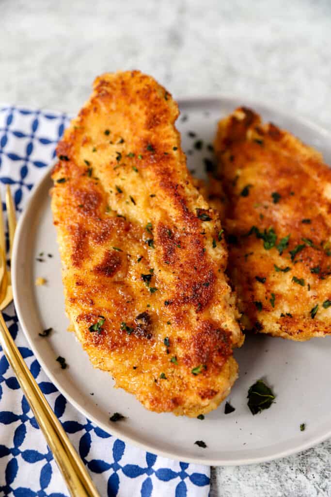 golden browned  cooked piece of chicken on a round great plate with a blue pattered napkin.