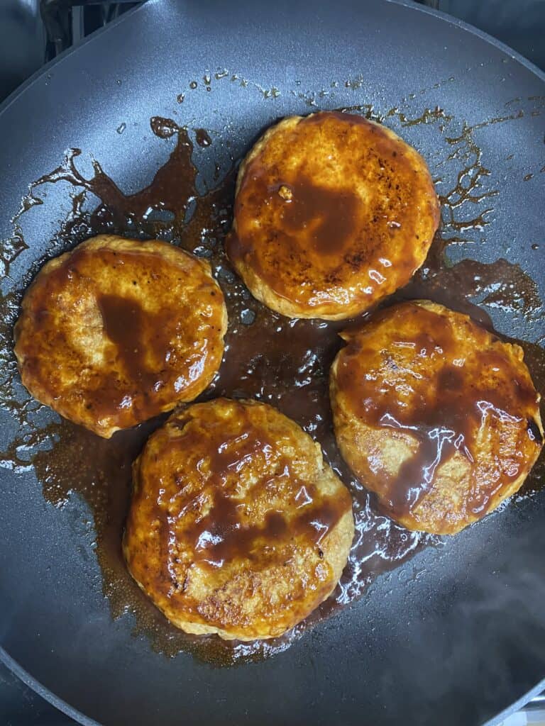 overhead shot cooking the chicken burgers in a pan with BBQ sauce