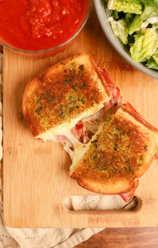 overhead shot of the Italian grilled cheese on a wood cutting board cut in half with cheese pulling apart.