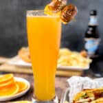 a beermosa on a wood surface with oranges and hotdog with chips