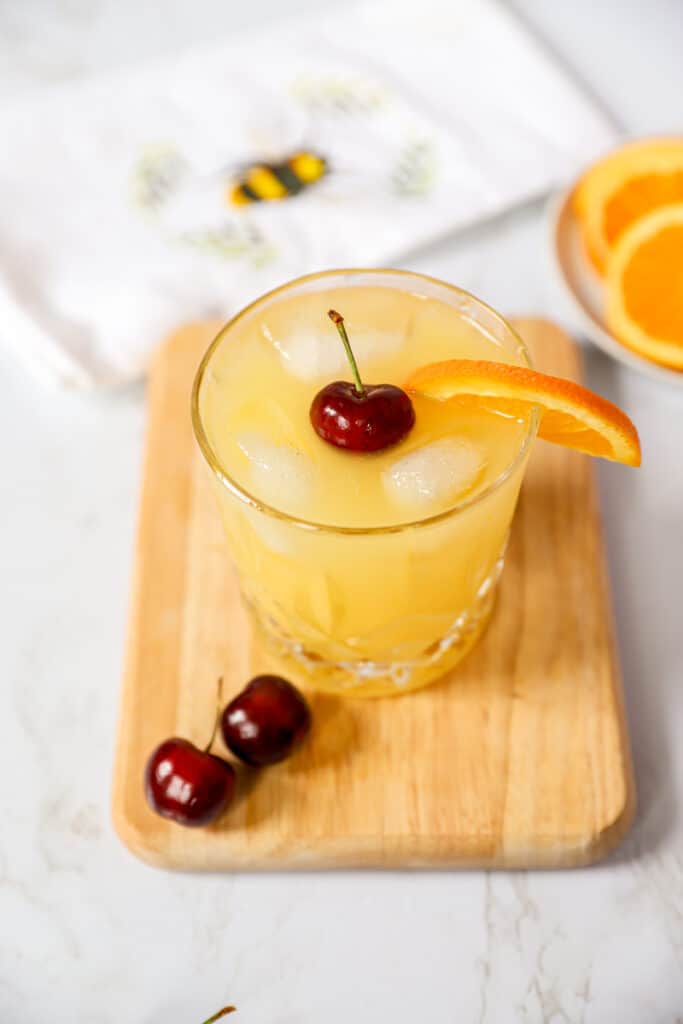 black eyed susan cocktail on a wood cutting board with fresh cherries.