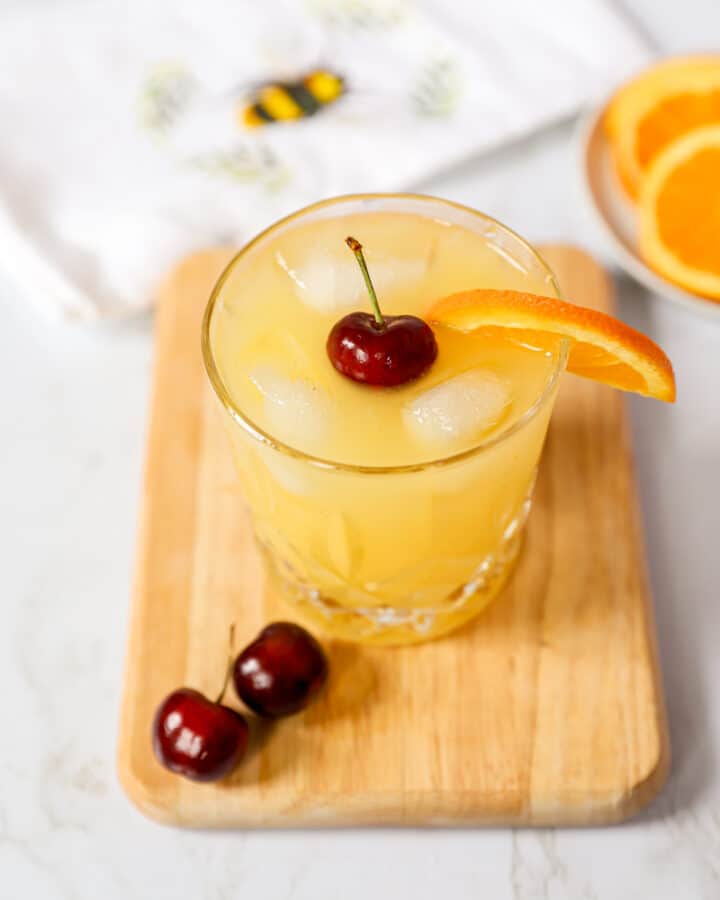 black eyed susan cocktail on a wood cutting board with fresh cherries.