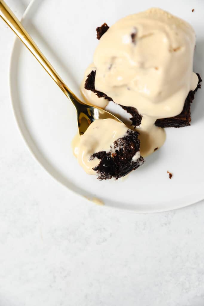 overhead shot of a gold spoon with the brownie and some coffee ice cream on a white plate.