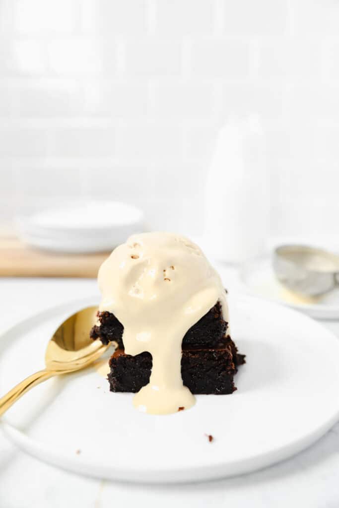 two brownies on a round white plate topped with coffee ice cream and a gold spoon