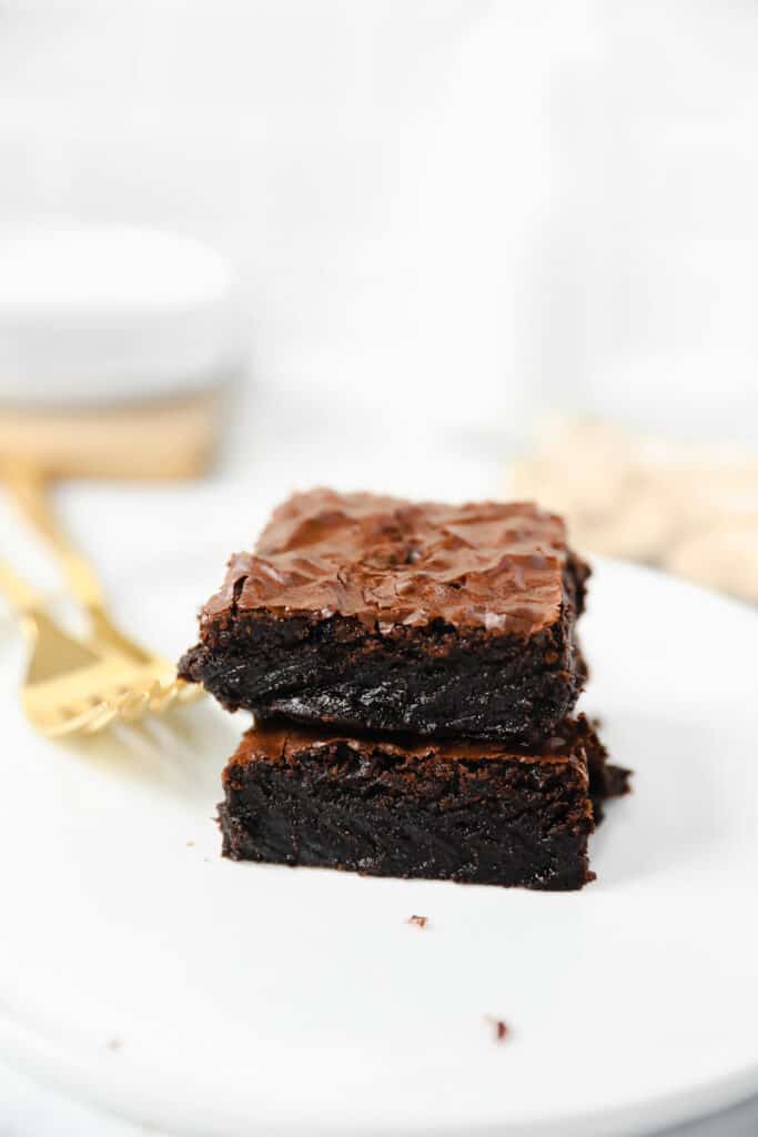 two fudgy doctored box brownies on a round white plate with two gold forks.