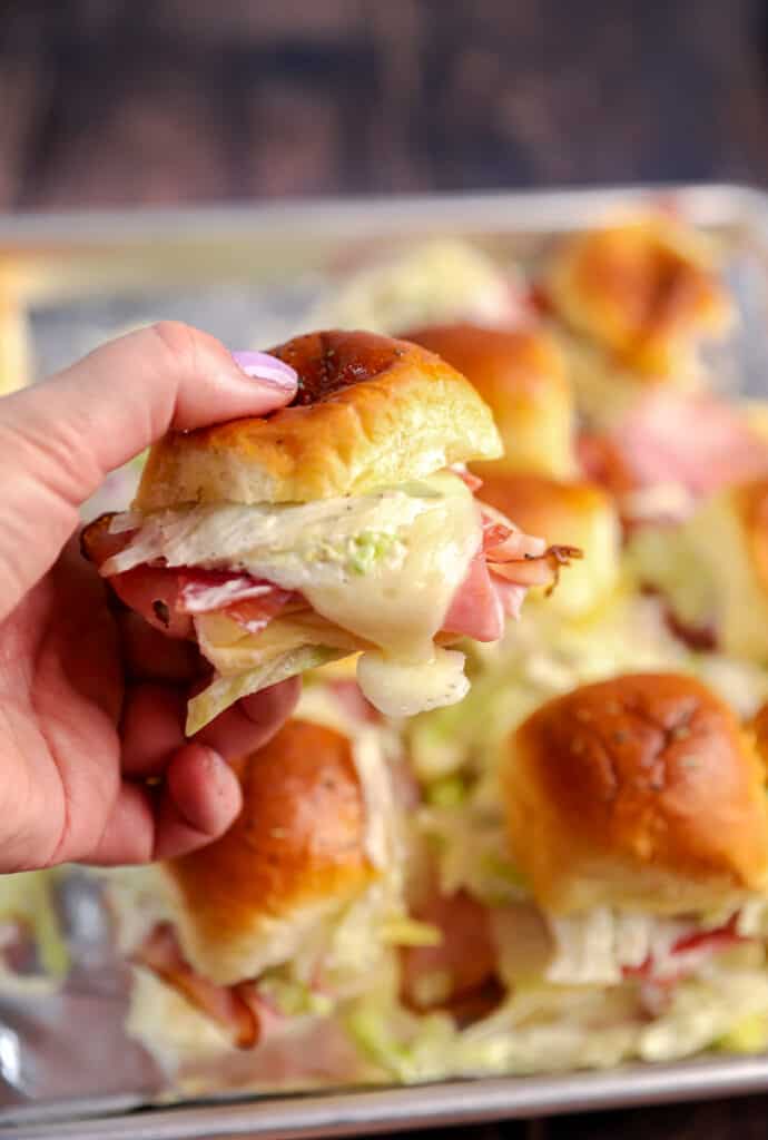 a hand holding one of the sub sliders close to the camera to show the melting cheese.