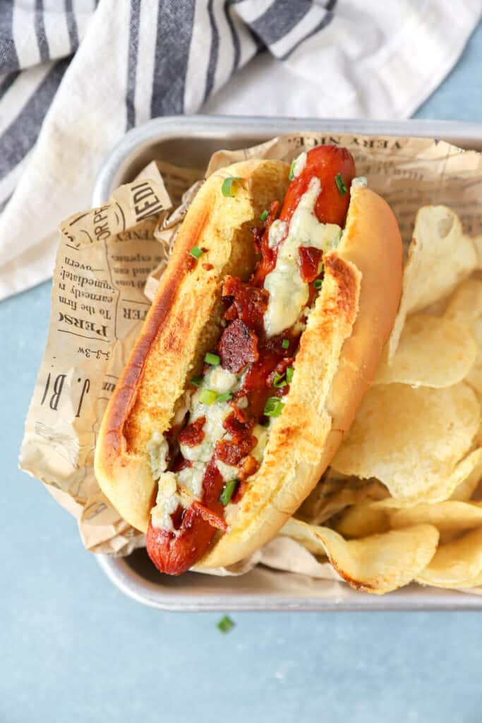 overhead shot of one of the hot dogs with chips in a silver serving tray with brown newsprint paper.