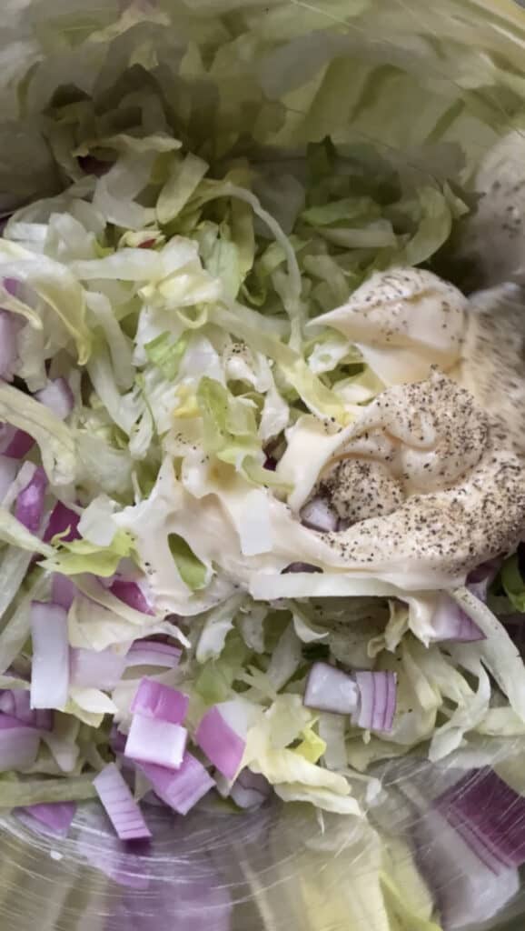 close shot of the shredded lettuce, diced red onions, mayo and pepper in a silver bowl.