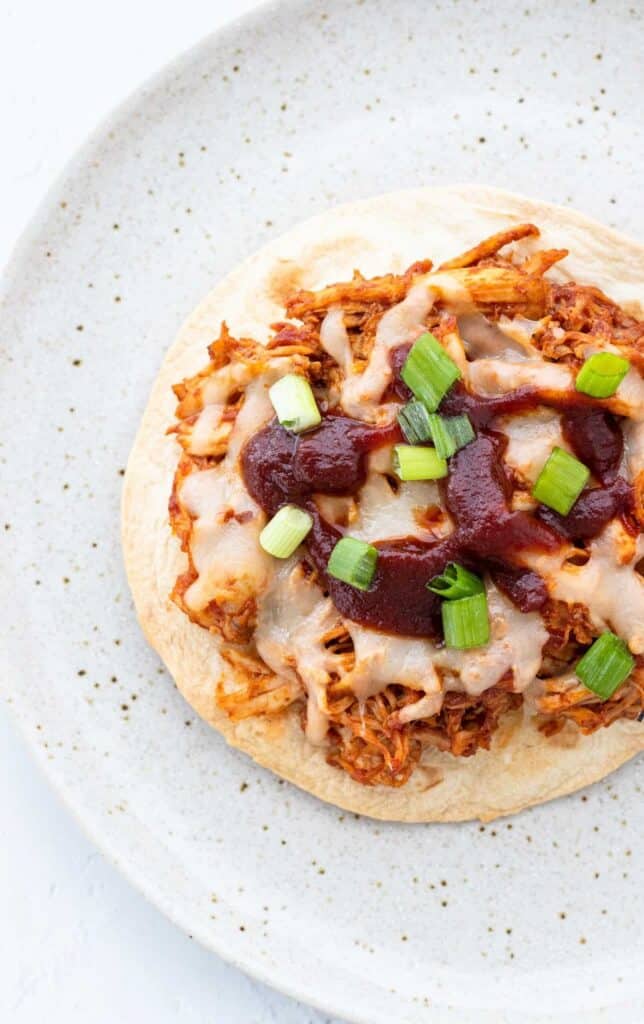 overhead shot of a BBQ chicken tostada topped with scallions on a speckled pattern plate.