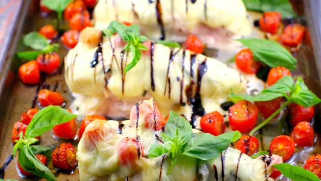 caprese chicken on a sheet pan drizzled with balsamic and fresh basil