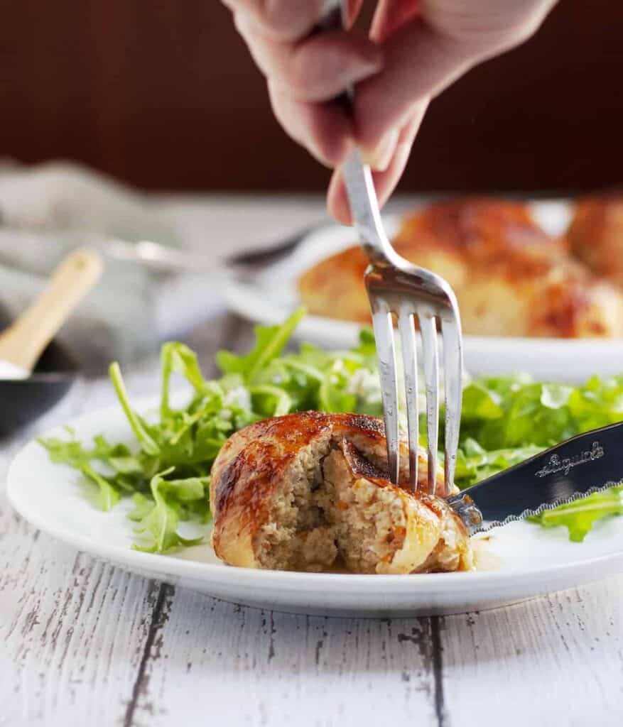 a fork and knife cutting a chicken ballotine on a plate with a green salad.