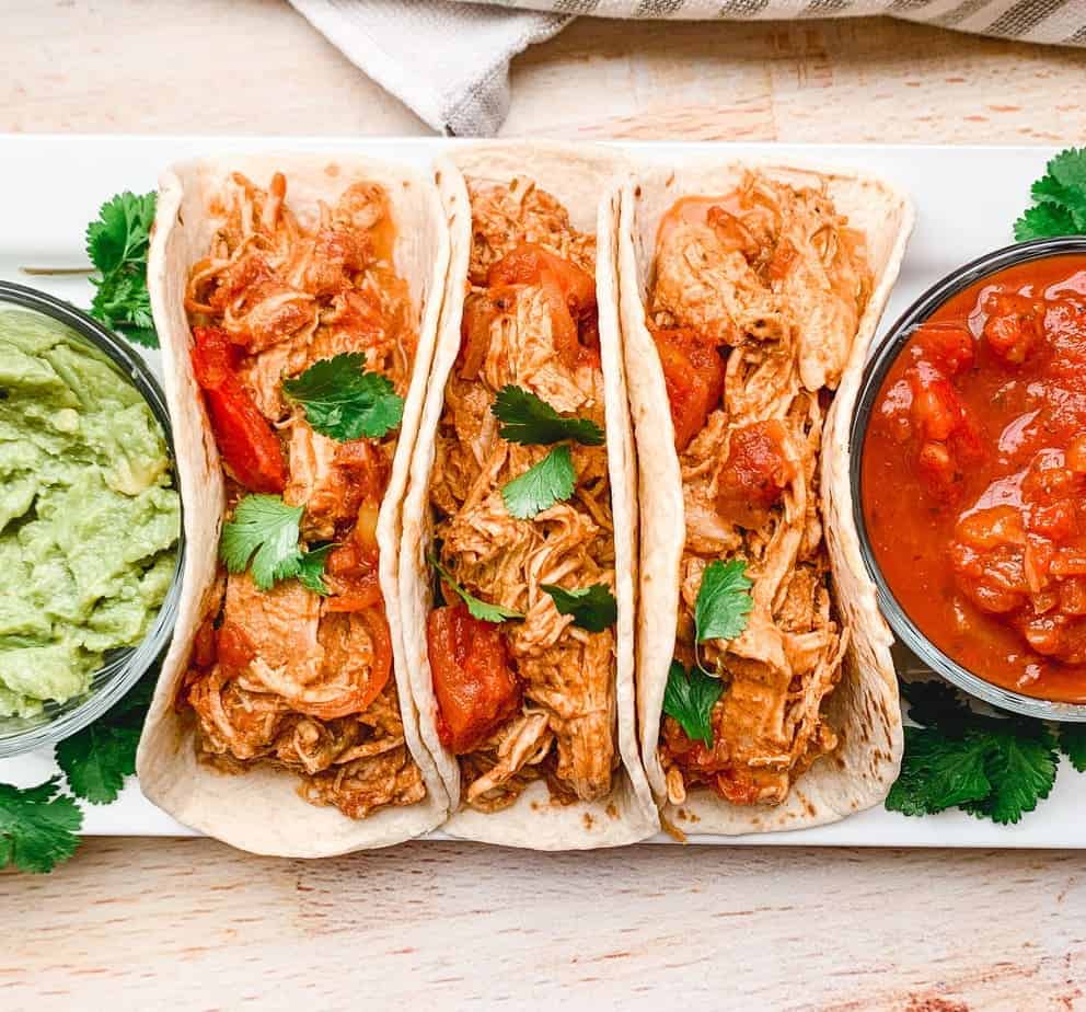 overhead shot of 3 chicken tacos with bowls of guac and salsa