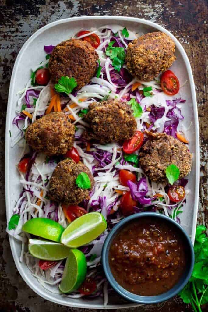 6 black bean croquettes on a dish with slaw and limes.