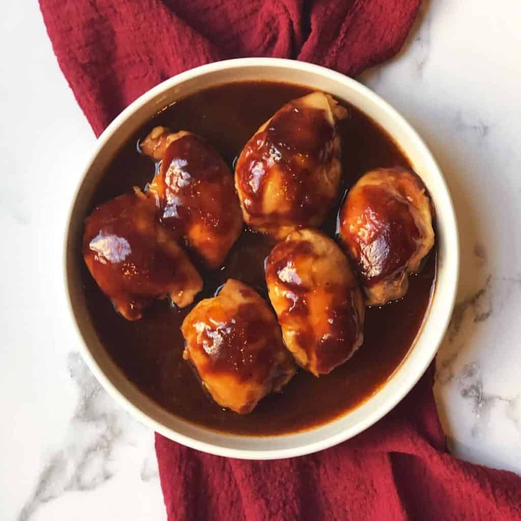 overhead shot of 6 chicken thighs in sauce in a white bowl