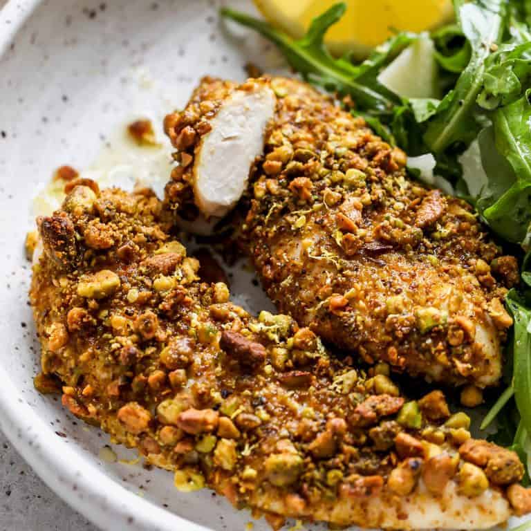 pistachio crusted chicken on a plate with a green salad.