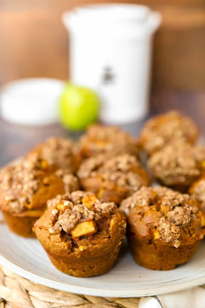 a plate of the pumpkin apple muffins with plates and a green apple in the background.