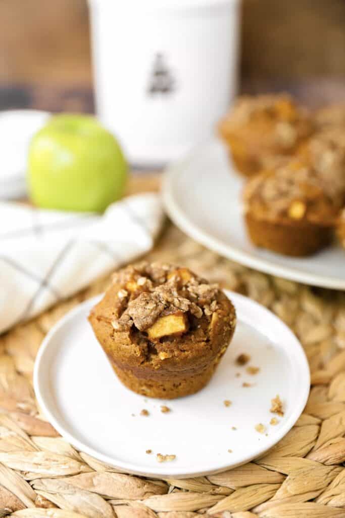 one pumpkin apple muffin on a white round plate on a rattan place mat.