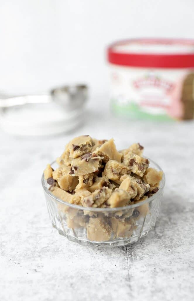 a small glass bowl filled with the no bake cookie dough pieces on a grey surface.