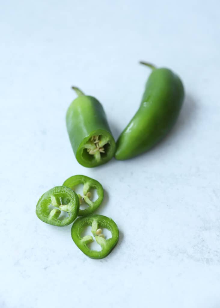 sliced and whole jalapeños on a grey surface