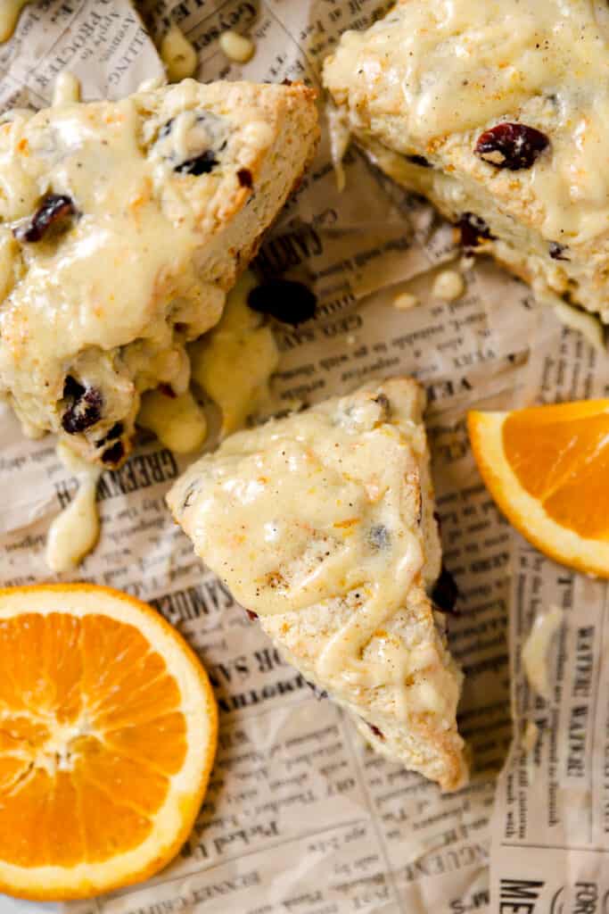 overhead shot of the orange cranberry scones on brown newsprint paper with orange slices