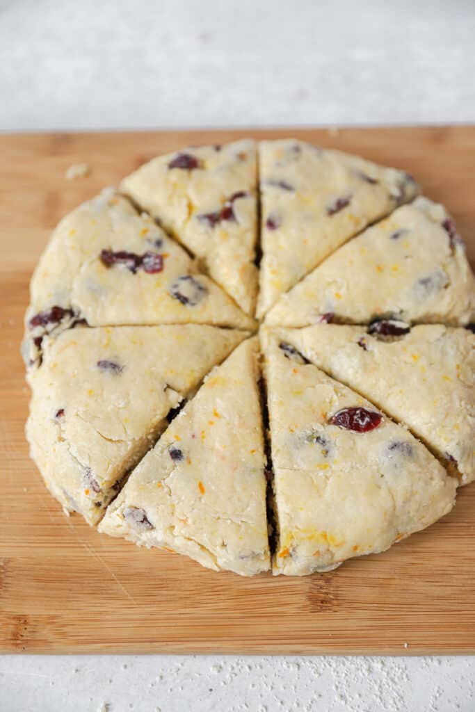 the circular scone dough on a wood cutting board cut into 8 triangle scones.