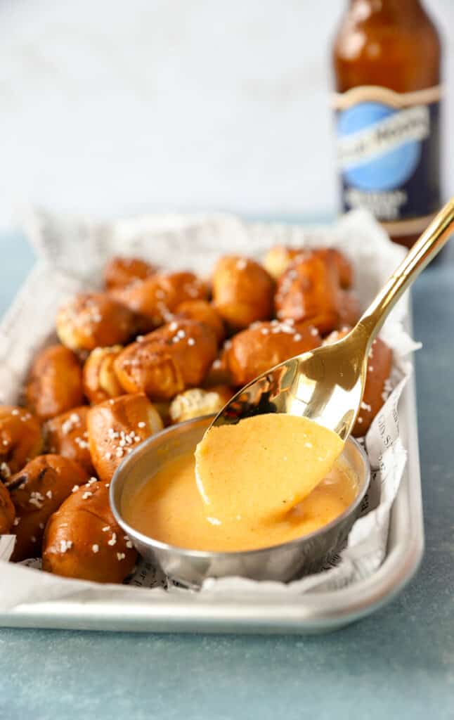 a gold spoon dipping into beer cheese sauce on a platter of pretzel bites.